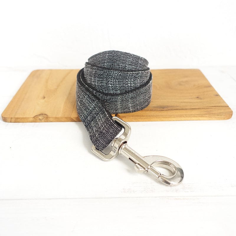 Laisse pour chien en tissu noir et argenté, présentée sur une planche en bois, idéale pour les promenades quotidiennes.