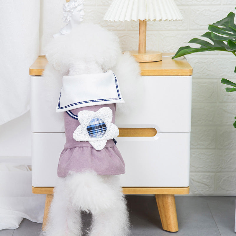 Chien portant une jupe à fleurs violette avec un motif floral, à côté d'une table moderne et d'une lampe.