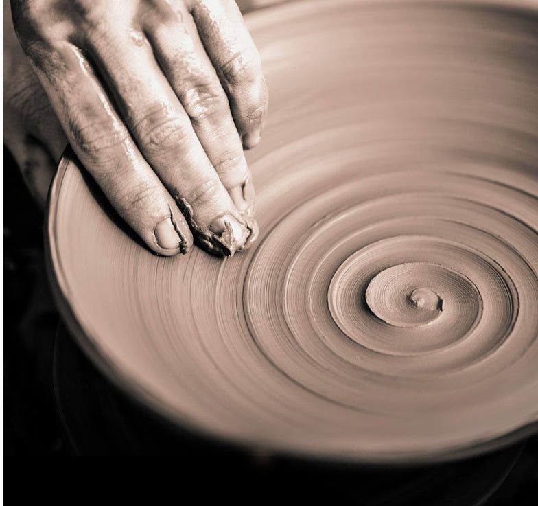 Artisan shaping clay on a pottery wheel, creating a circular design.