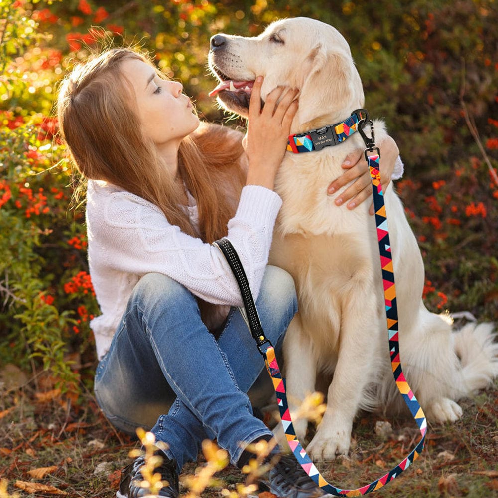 Une jeune femme caresse un golden retriever, portant un collier coloré et une laisse, entourés de fleurs en pleine nature.