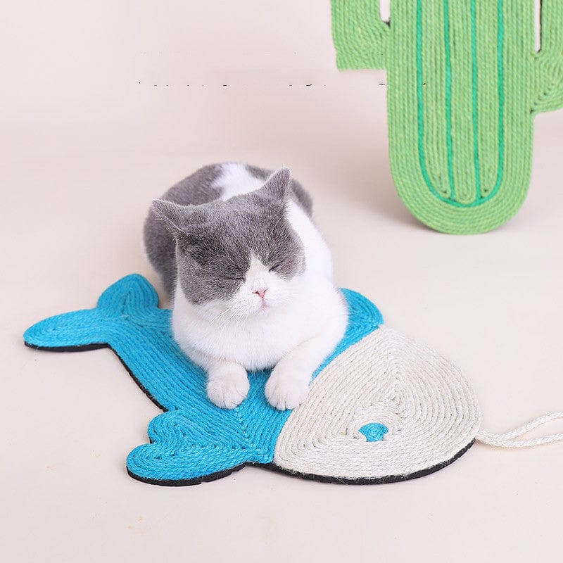 Chat allongé sur un tapis à gratter en sisal en forme de poisson, à côté d'un cactus décoratif.