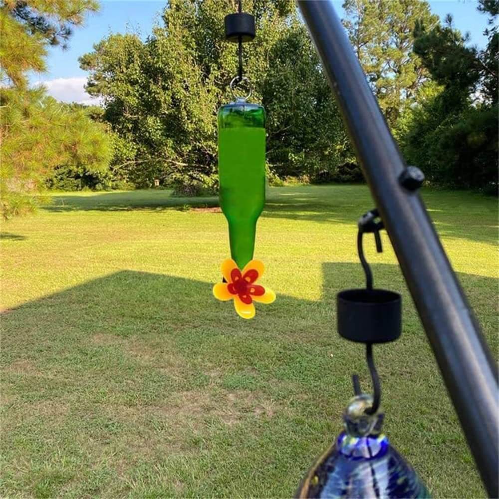 Distributeur de graines pour oiseaux en bouteille de vin avec décoration florale, jardin verdoyant en arrière-plan.