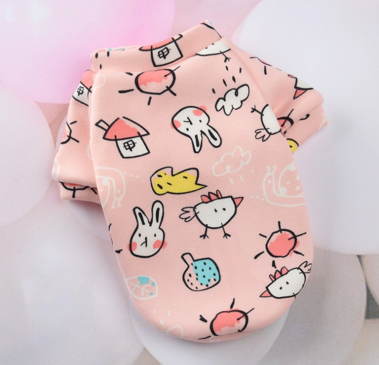Vêtement pour petits chiens en tissu rose avec motifs colorés de maisons et animaux.
