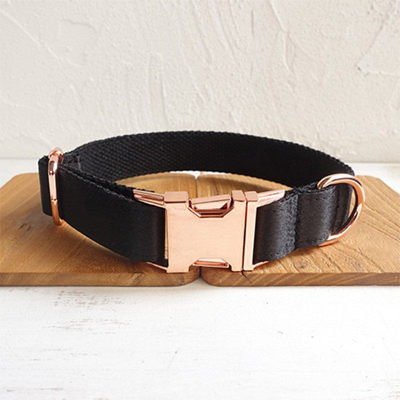 Collier pour chien noir en polyester avec boucle dorée sur un fond en bois.