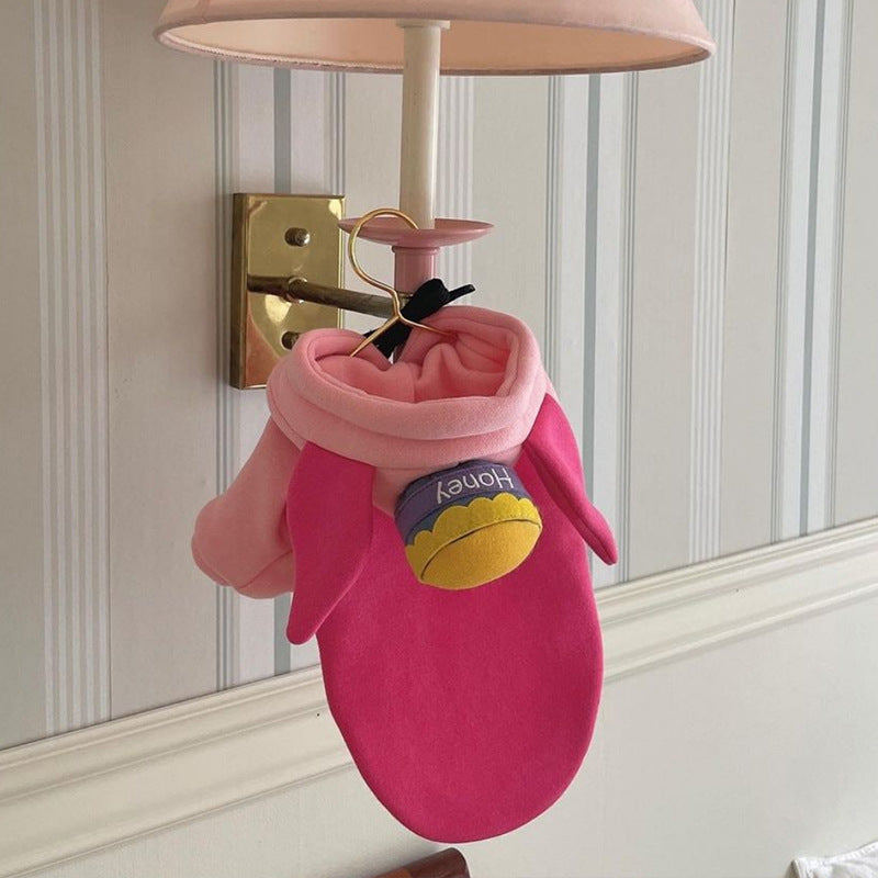 Vêtement color block pour chien en rose, avec oreilles et étiquette, accroché à une lampe.