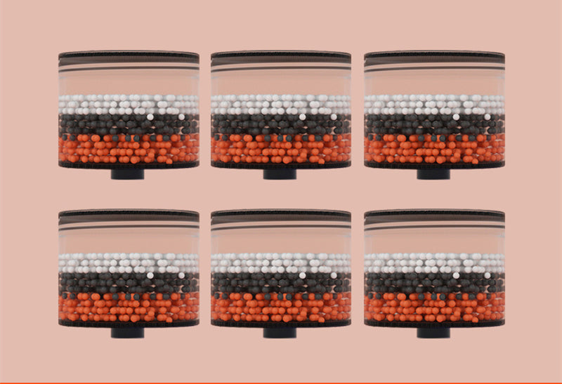 Six transparent canisters filled with vibrant orange, black, and white beads against a soft pink background.