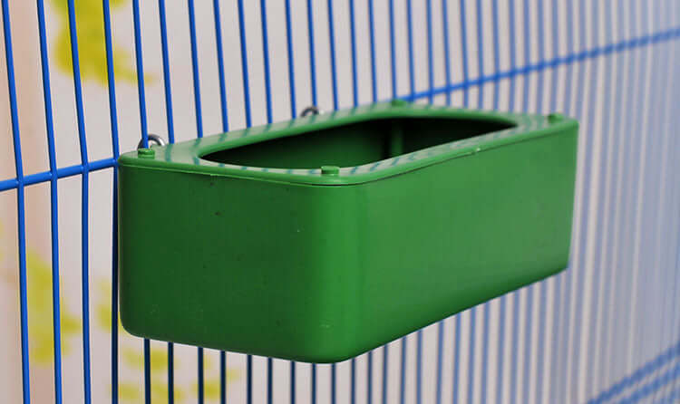 Conteneur de nourriture pour oiseaux vert suspendu dans une cage, idéal pour garder la nourriture propre.