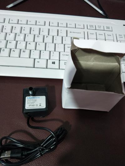 Automated water fountain pump with box and USB cable, placed next to a keyboard.