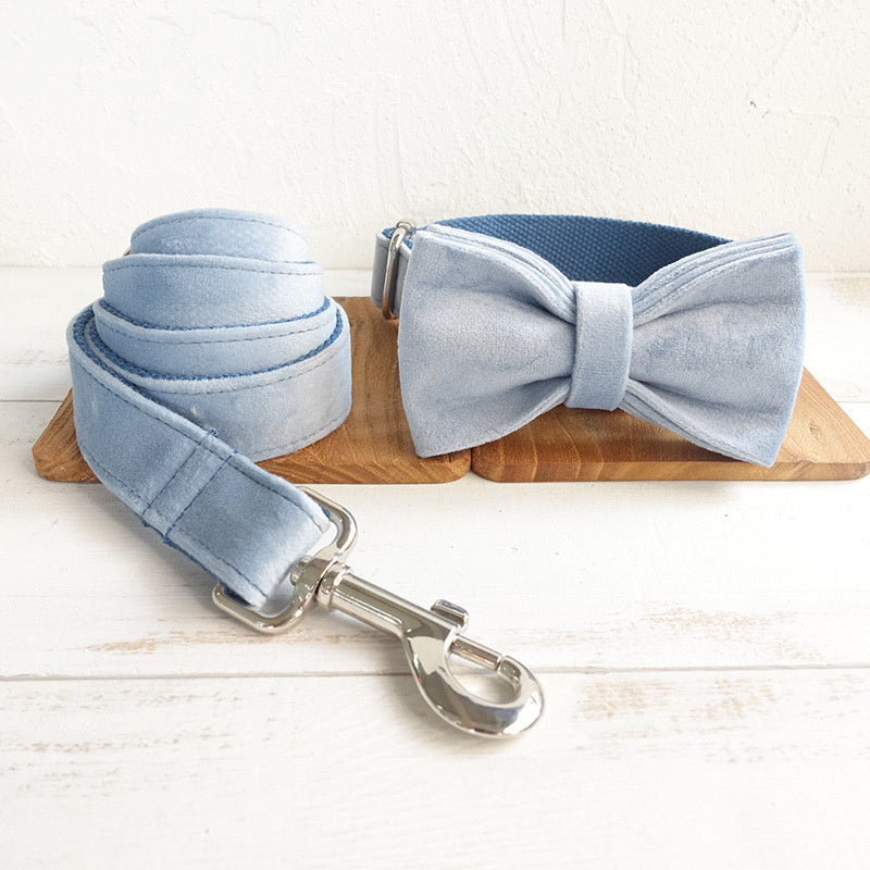 Collier pour chien bleu en velours avec nœud papillon et laisse assortie sur un support en bois.