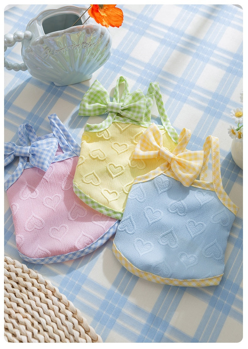 Colorful heart-patterned pet overalls in pink, yellow, and blue for small dogs on a checkered tablecloth.