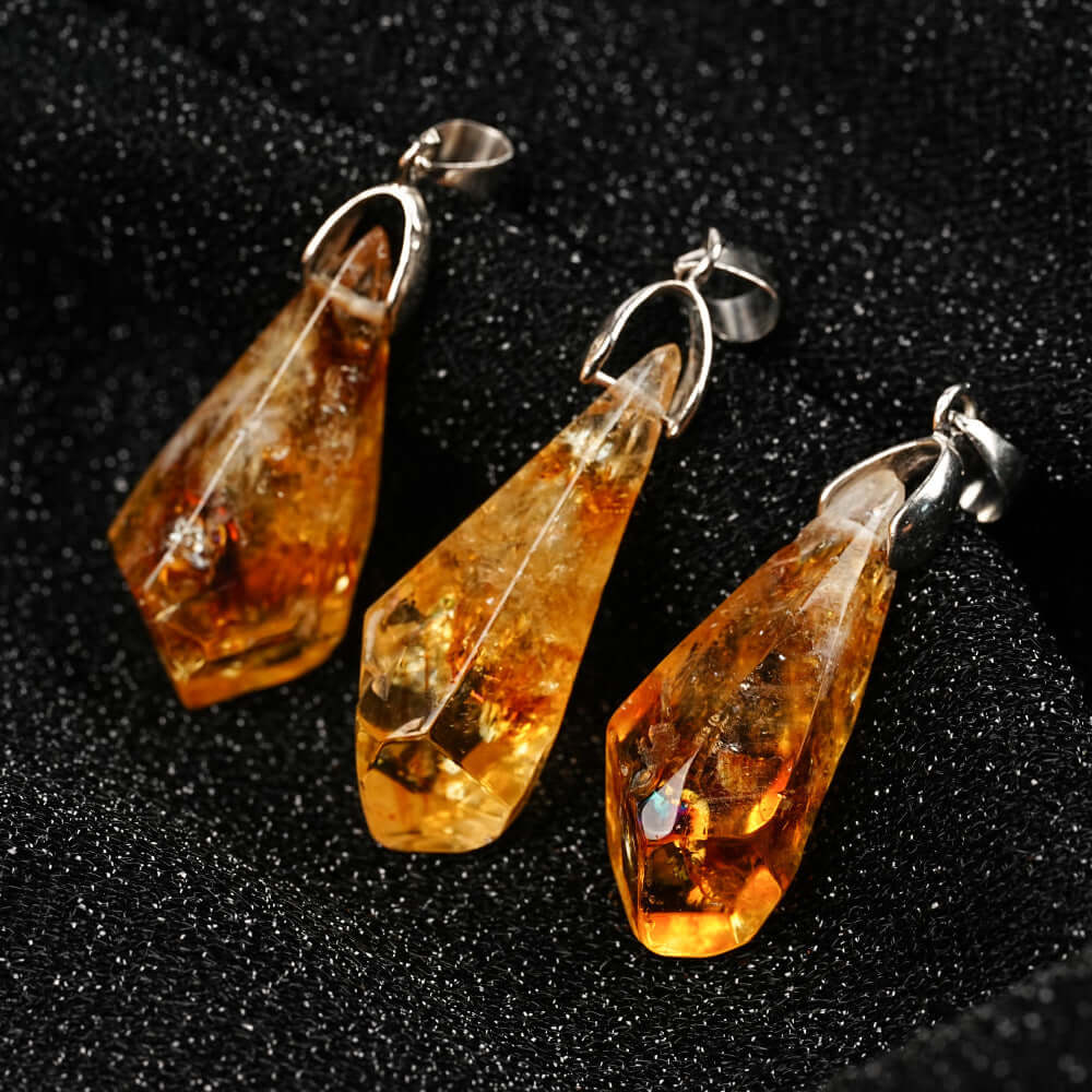 Pendentifs en citrine naturelle avec des éclats dorés, suspendus sur un fond noir.