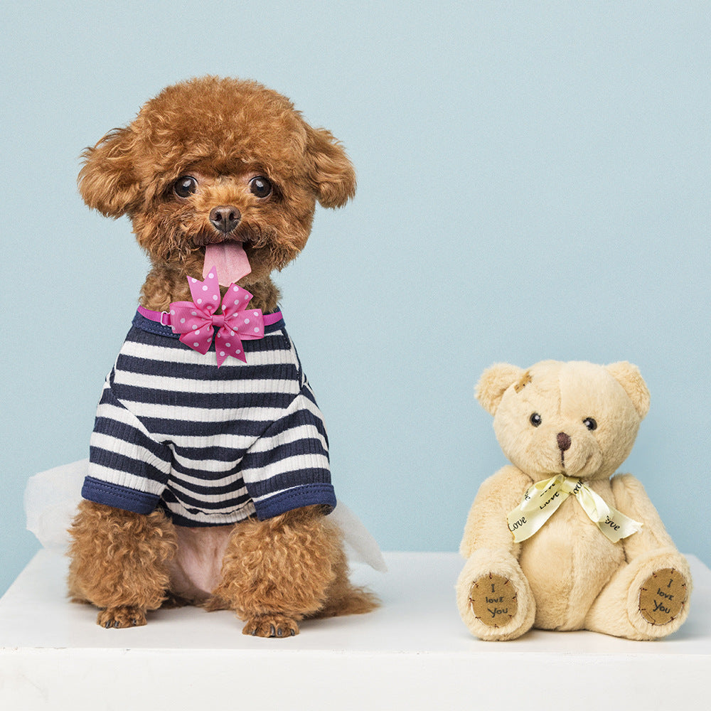 Un adorable chien en pull rayé avec un nœud papillon, posé à côté d'un ours en peluche.