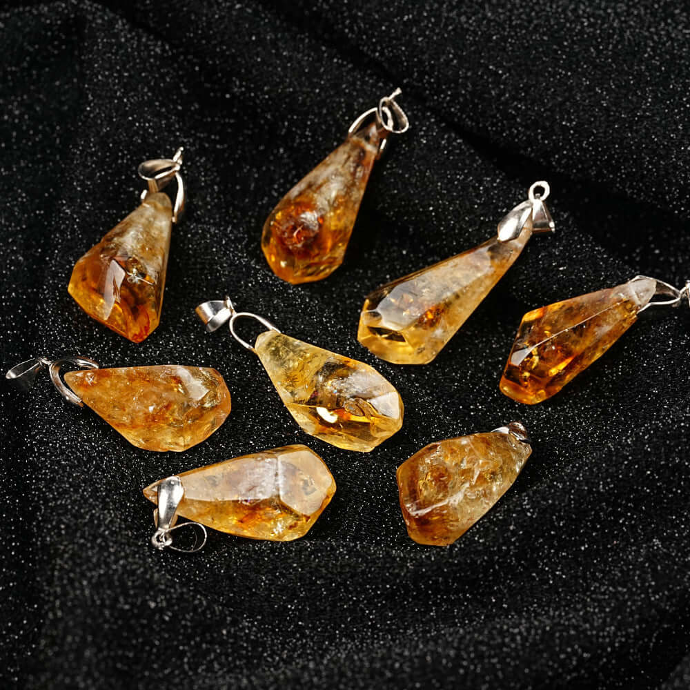 Pendentifs en citrine naturelle aux formes irrégulières, suspendus sur un fond noir pour un éclat doré unique.