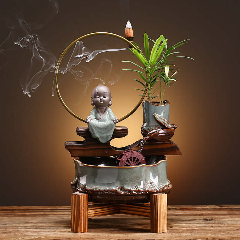 Décoration zen avec statue de méditation, plante, et source d'eau pour ambiance apaisante dans votre espace.