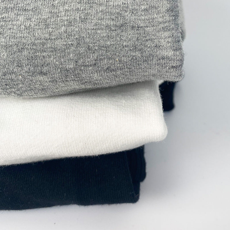 Trois pulls à capuche en coton pour chien, disponibles en gris, blanc et noir, empilés sur une surface neutre.