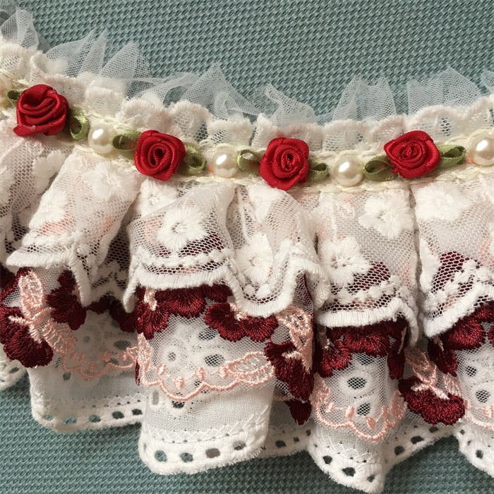 Détails d'un bavoir en coton avec nœud en dentelle, ornements de fleurs rouges et perles délicates.