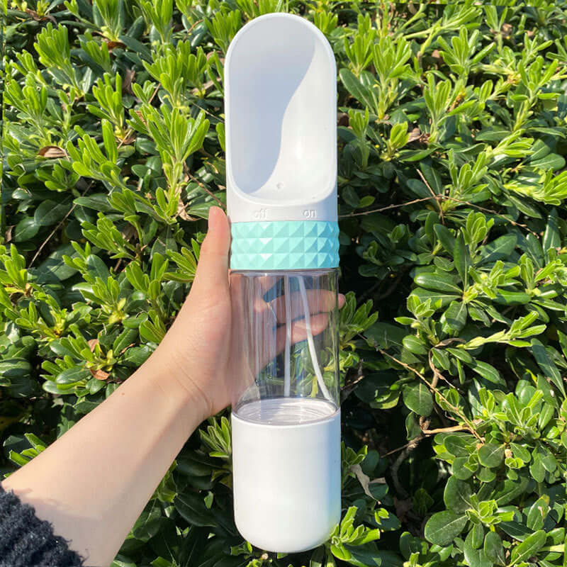 Gobelet d'eau portable pour chien, idéal pour les aventures en extérieur, en main près d'arbustes verts.