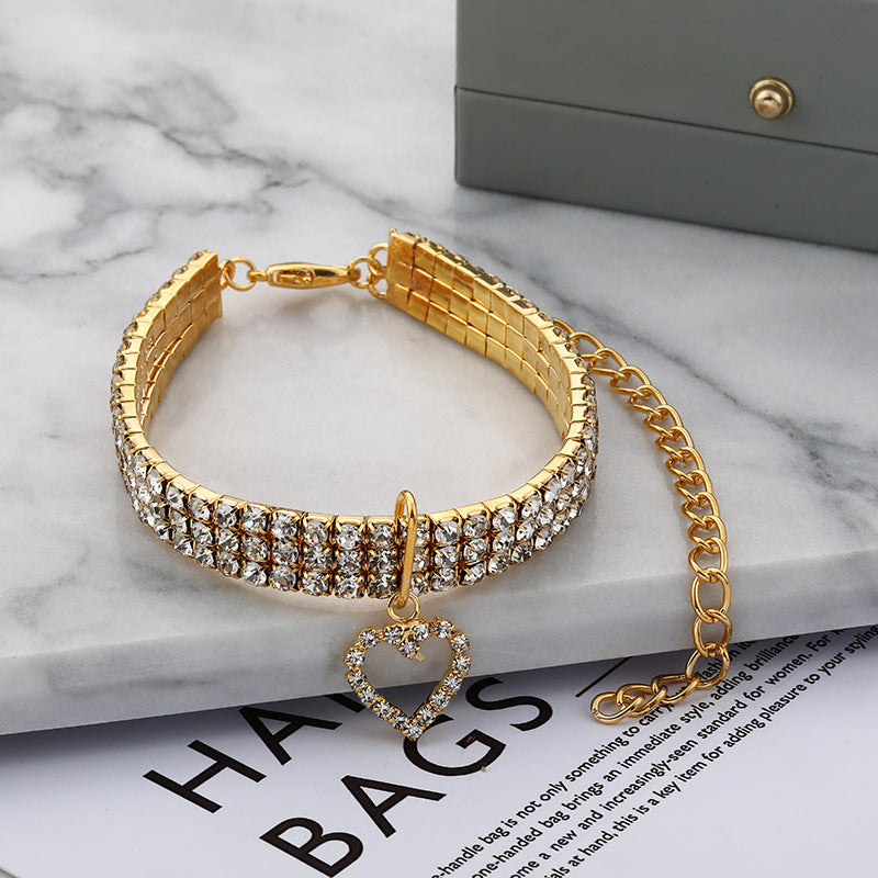 Collier en strass doré à trois rangées avec pendentif cœur pour animaux de compagnie sur une table en marbre.