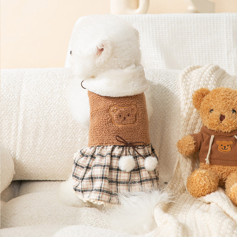 Petit chien portant une robe ourson mignonne avec une jupe en plaid, assis sur un canapé.