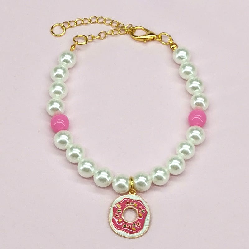 Bracelet en perles blanches avec pendentif donut rose et perles roses, parfait pour un look ludique et coloré.