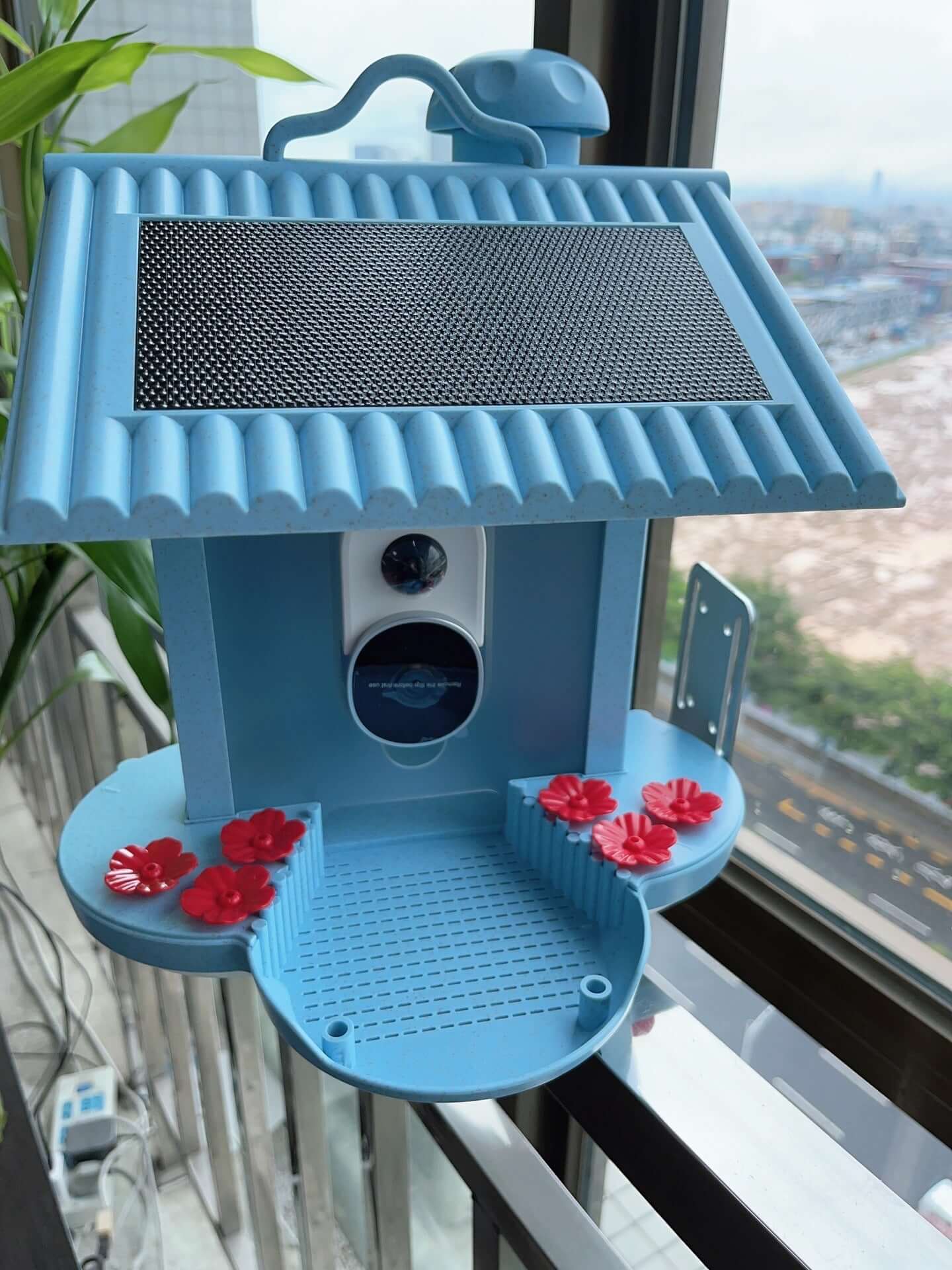 Vue du Distributeur Intelligent d’Oiseaux 160° bleu avec fleurs décoratives, conçu pour nourrir les oiseaux.