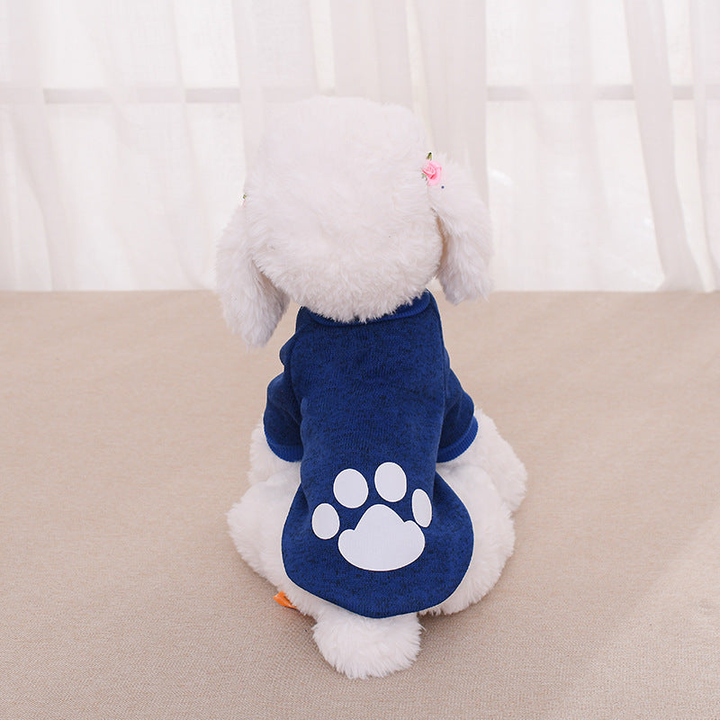 Chien en peluche portant un pull bleu avec motif de patte, vue arrière sur un fond neutre.