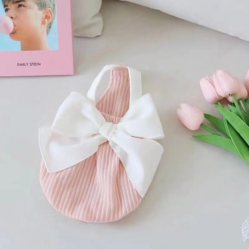 Salopette d'été pour chien rose avec nœud blanc sur une table décorative, idéale pour les sorties estivales.