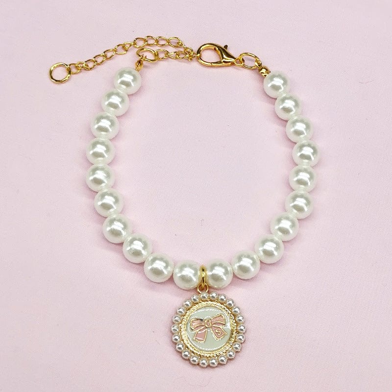 Collier festif pour animal avec perles blanches et pendentif décoratif en forme de nœud.