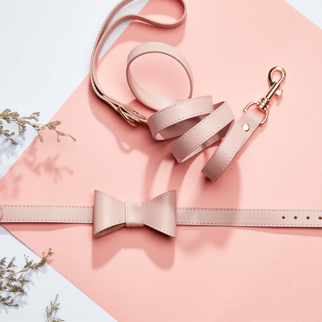 Ensemble collier et laisse pour animaux avec noeud en cuir rose sur fond rose, idéal pour les promenades avec style.