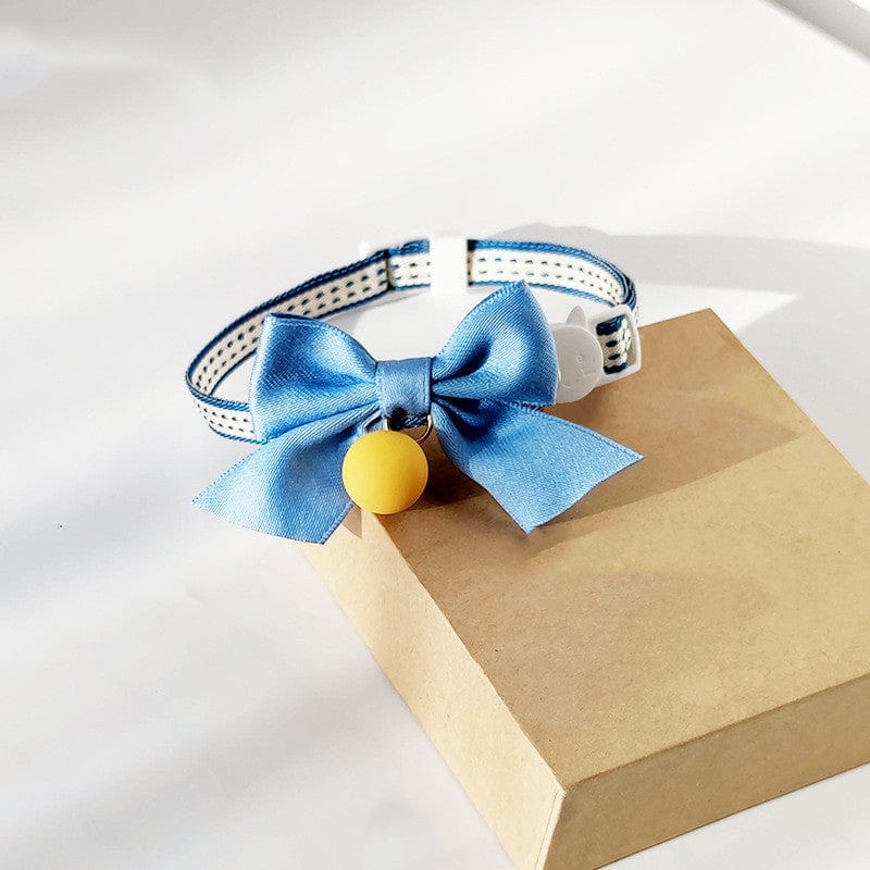 Nœud papillon bleu avec cloche pour chat, accessoire élégant sur fond de boîte marron.