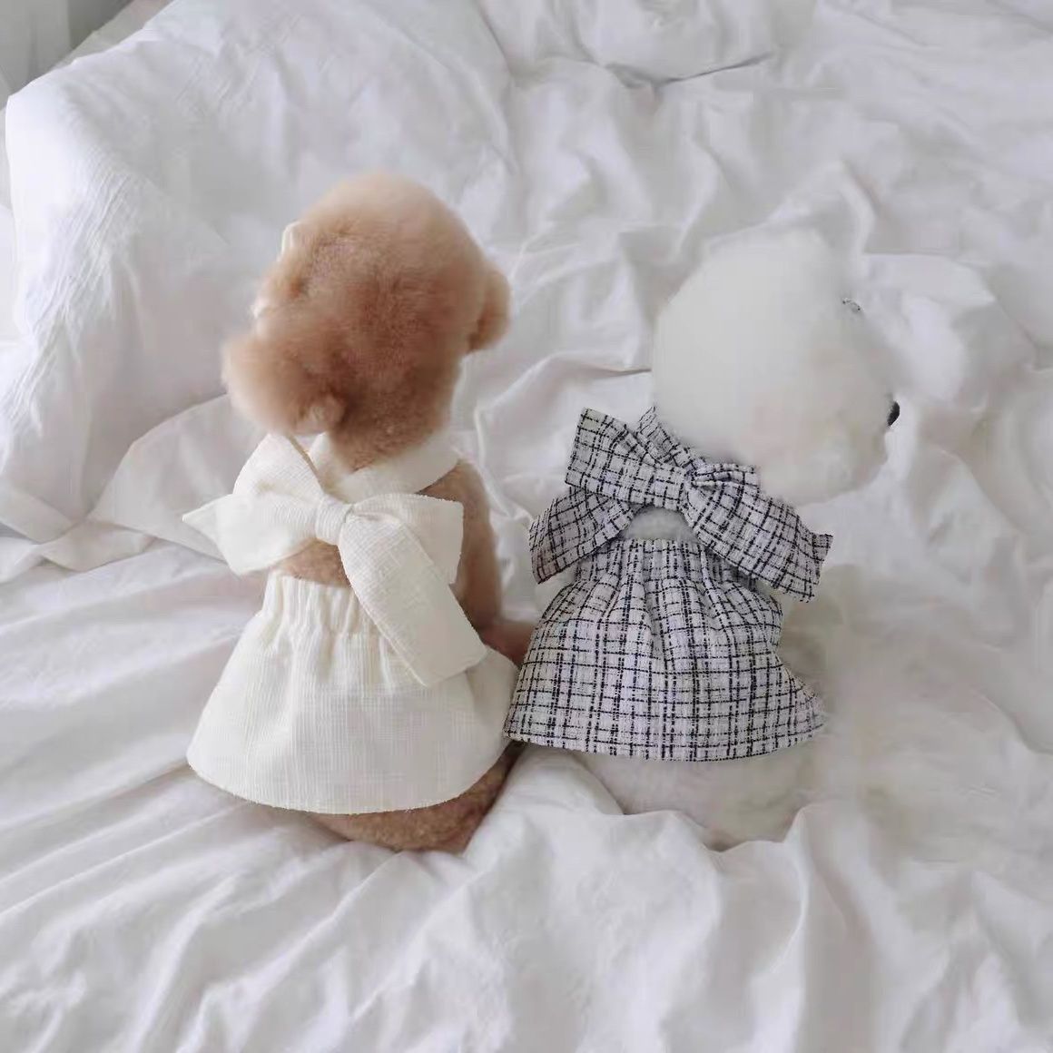 Deux chiens en peluche portant des jupes élégantes avec des nœuds, sur un lit en désordre.
