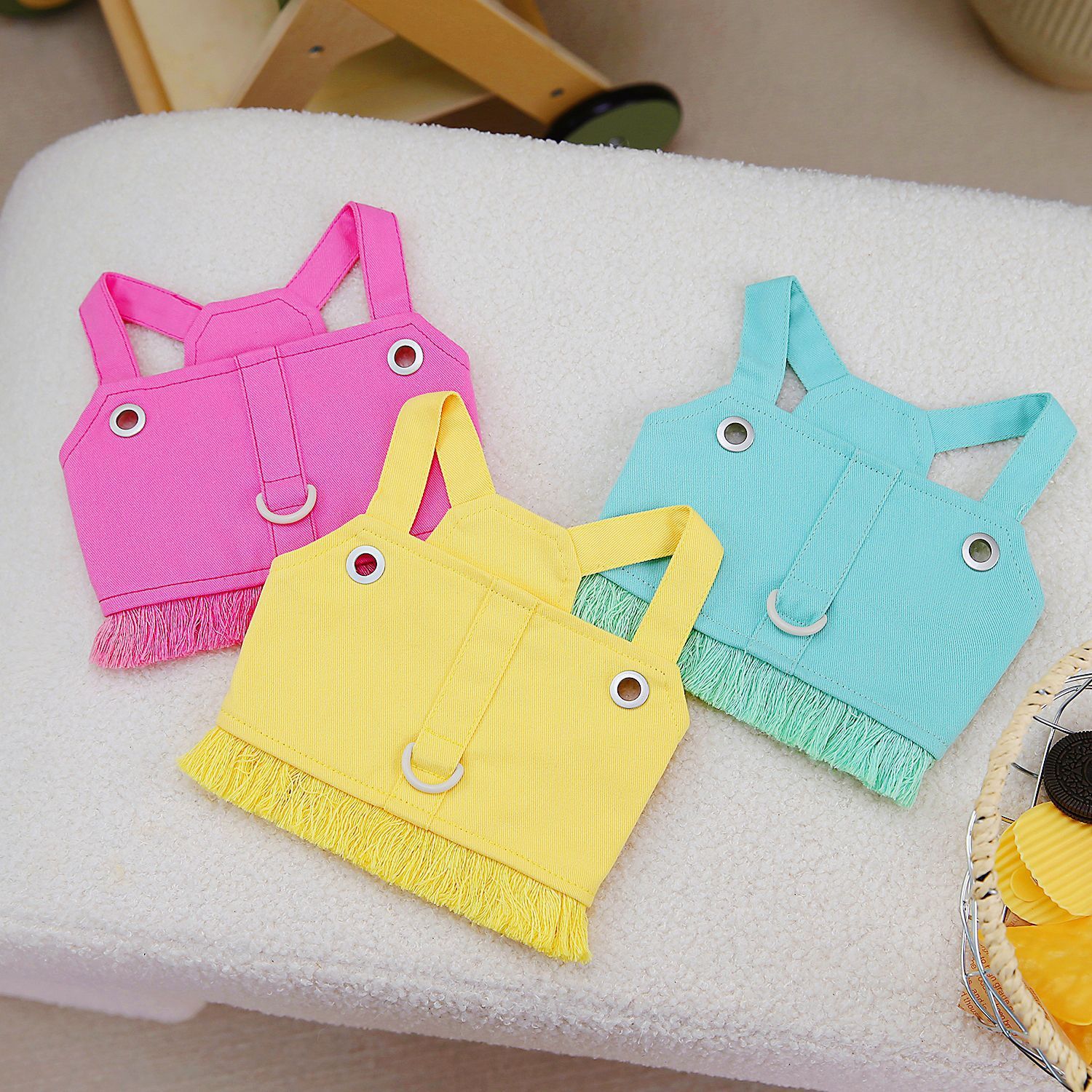 Trois harnais de traction personnalisés pour animaux en rose, jaune et vert clair, avec détails en franges.